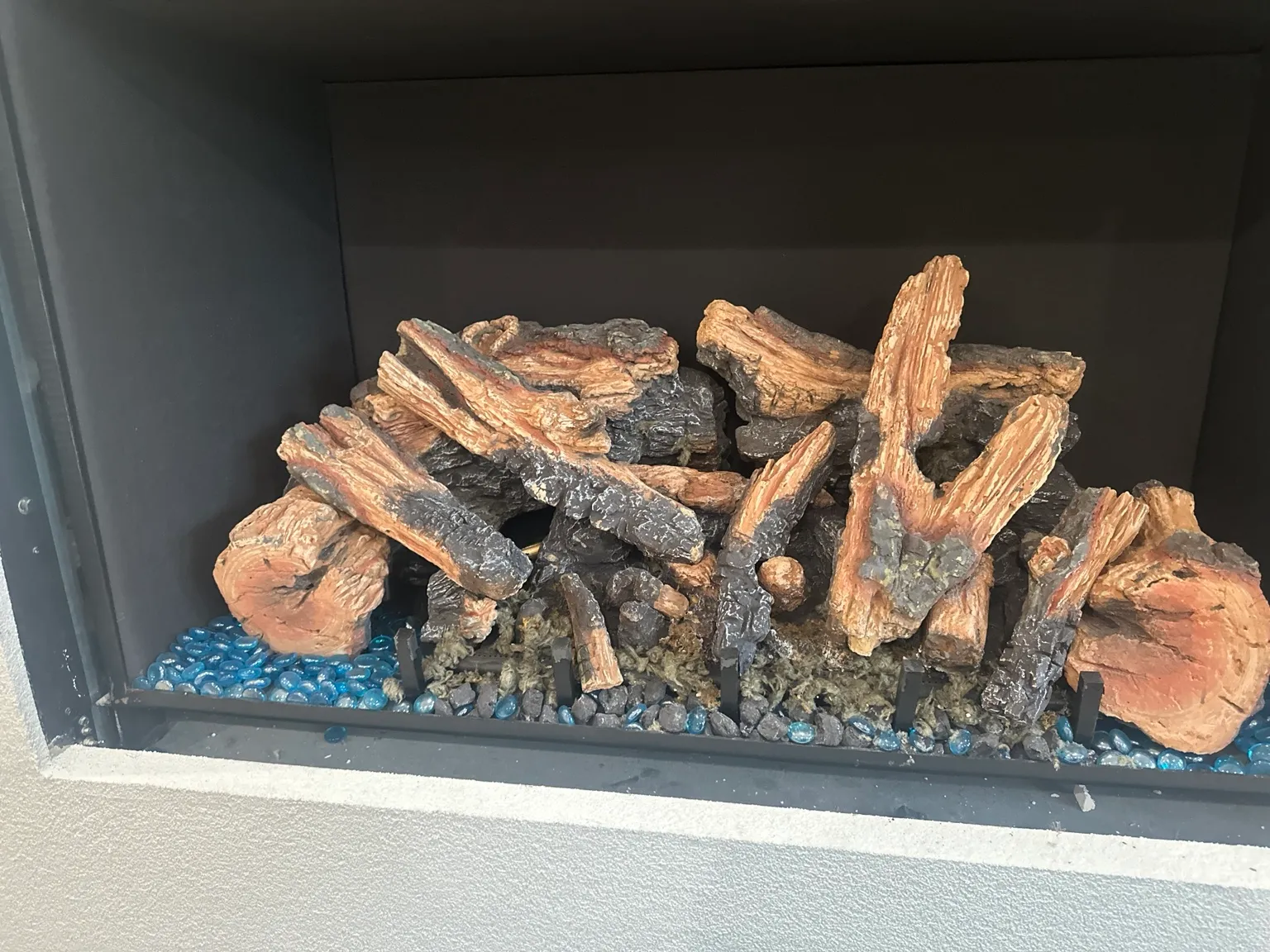 Gas log set in a black firebox with blue decorative glass along the base.