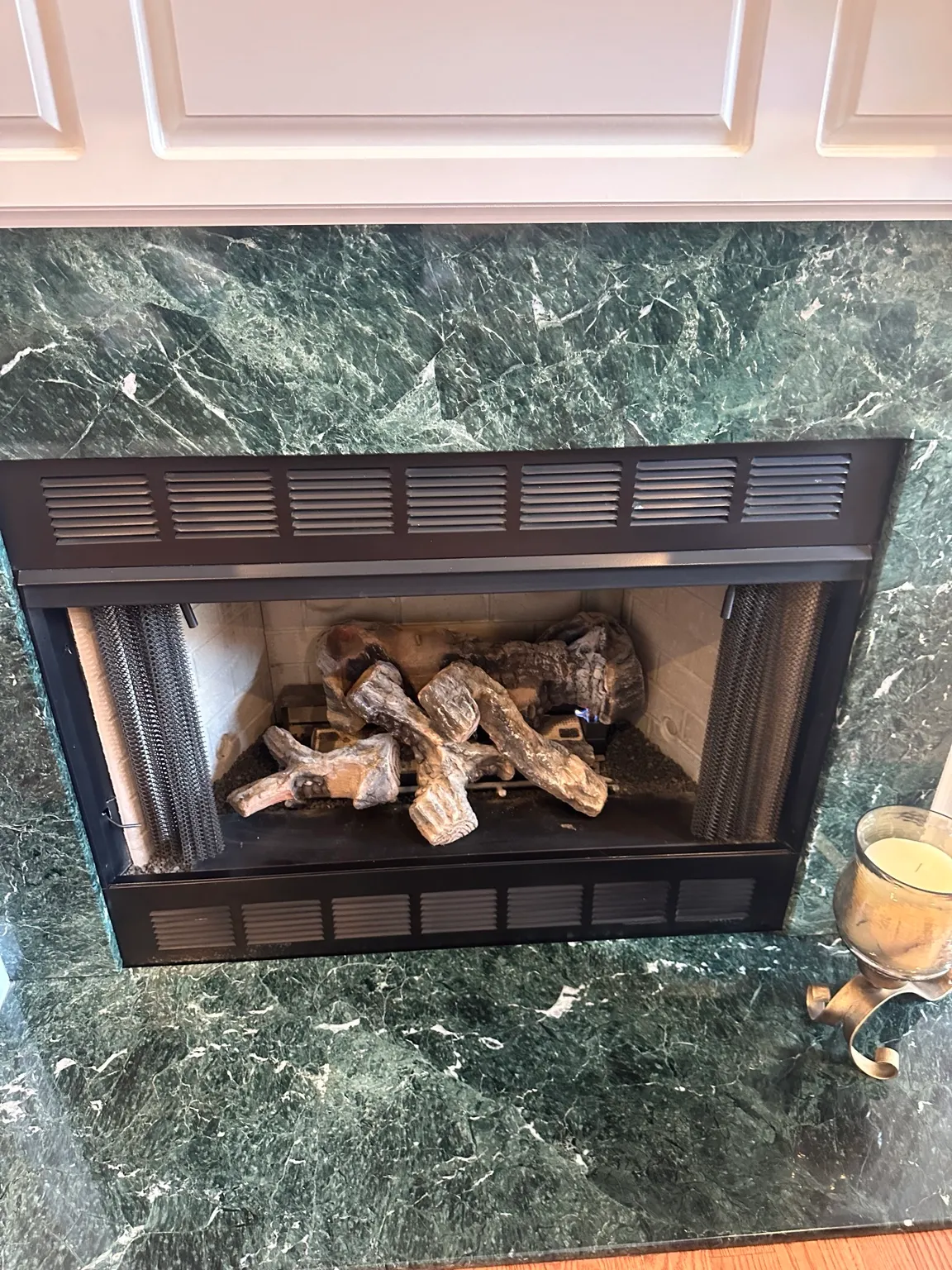 Gas log set inside a black louvered firebox, set into a green marble surround.