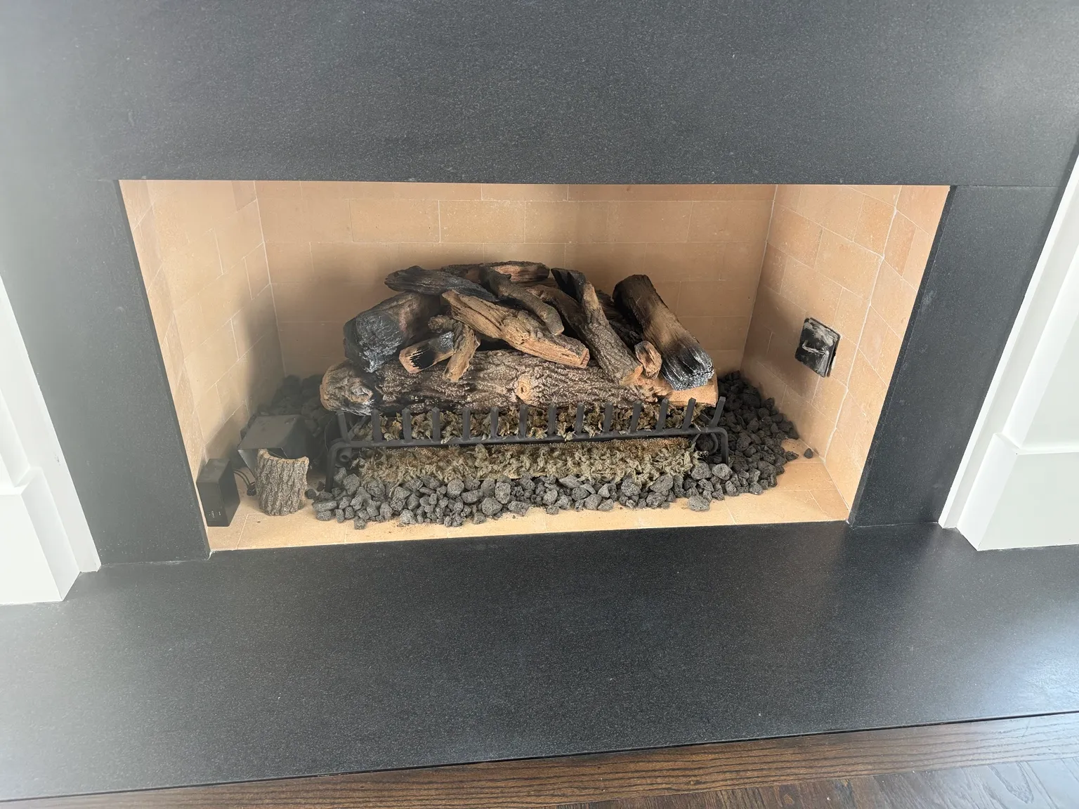 Wide gas log set on a grate over lava rock, in a tan firebox with a dark stone surround.