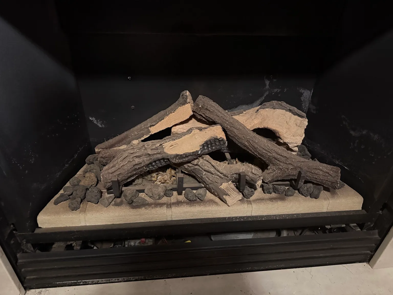 Unlit ceramic gas log set resting on a burner inside a black firebox.