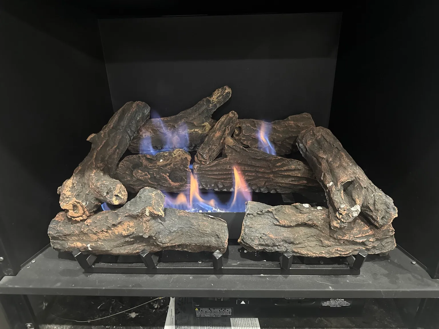 Gas logs burning with blue and orange flame inside a dark firebox.