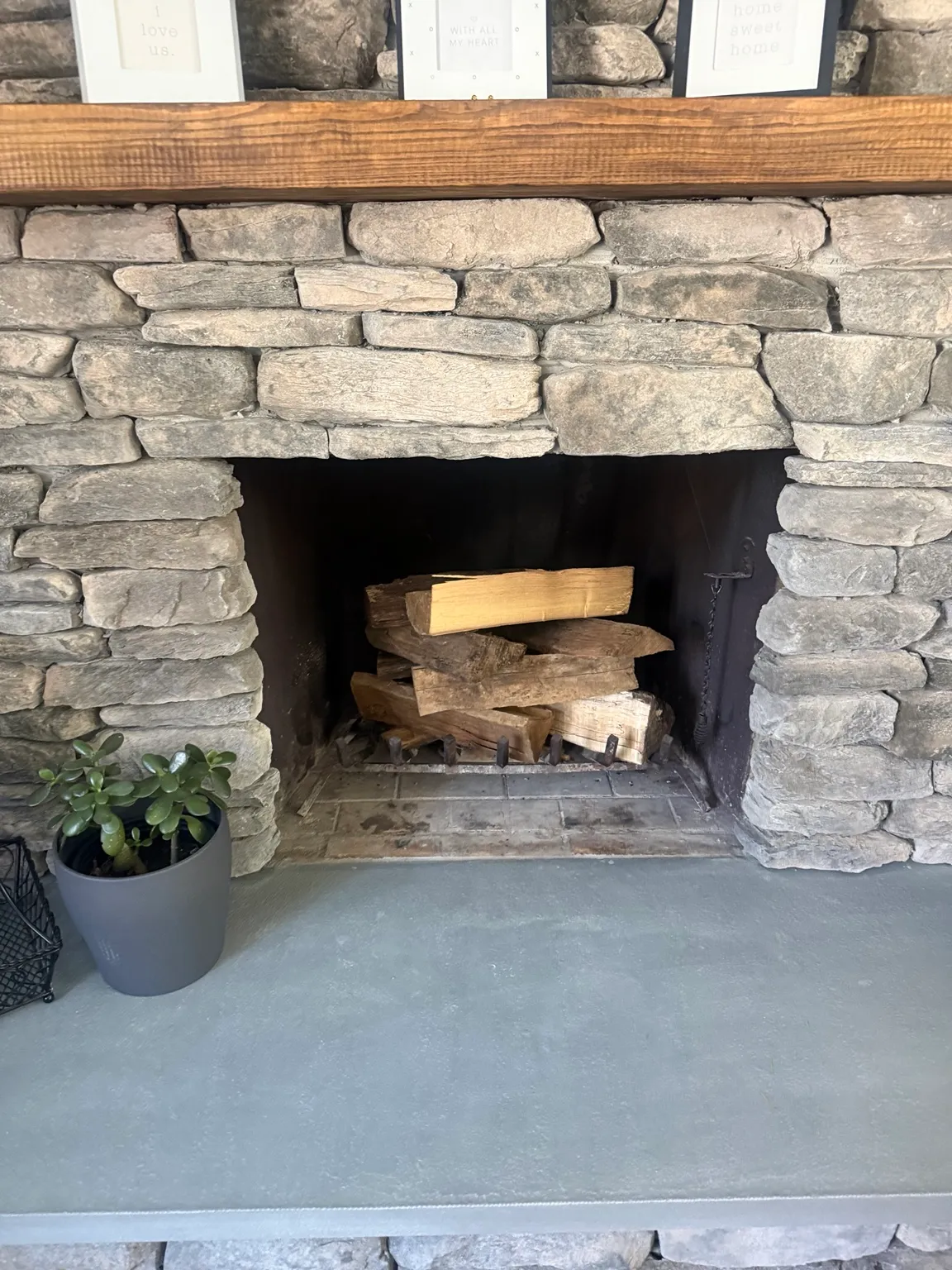 Stacked stone fireplace with a rustic wood mantel and split firewood in the firebox.