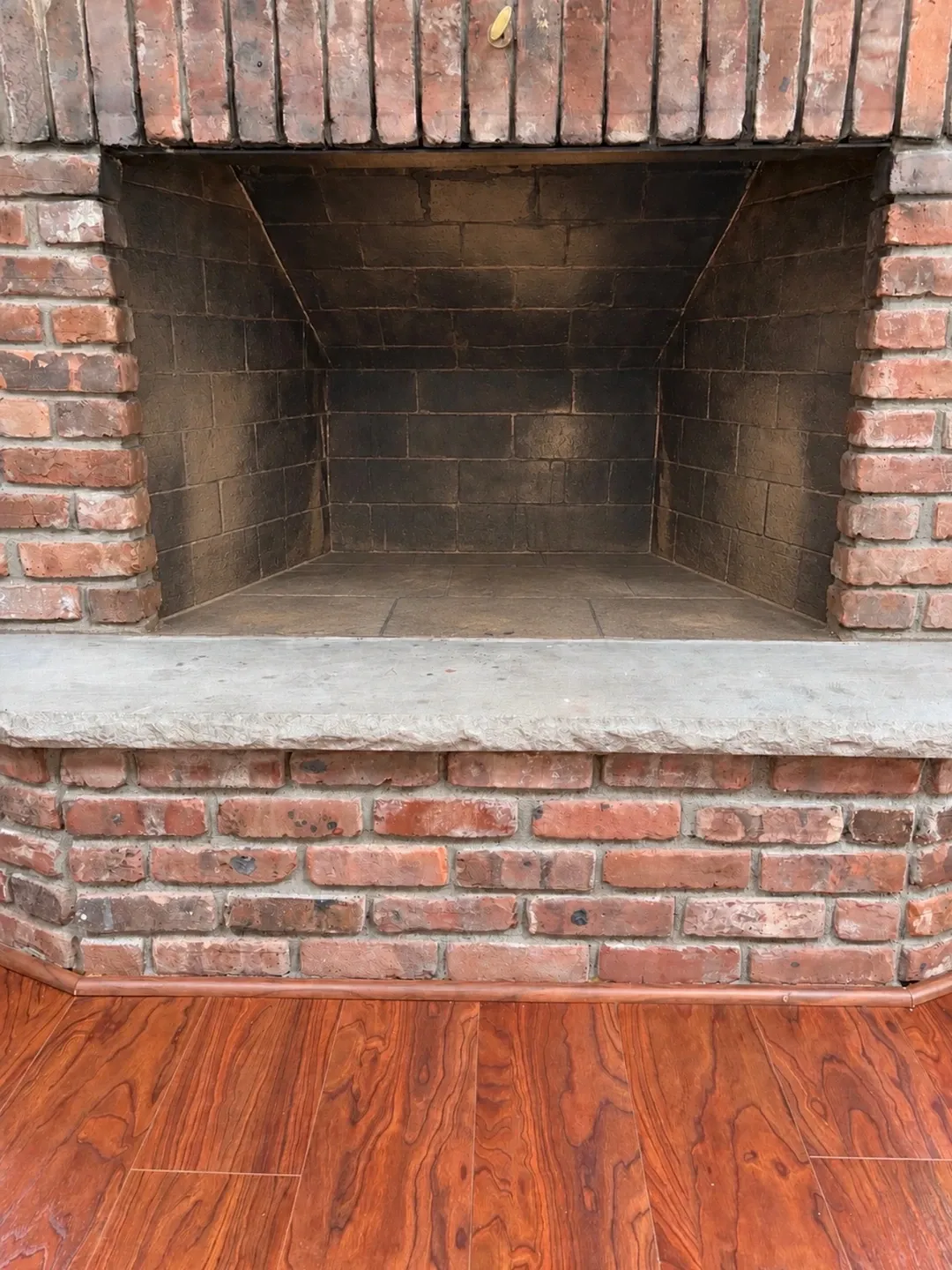 Empty firebox in a red brick fireplace, its soot-darkened masonry interior above a concrete hearth slab and a brick base.